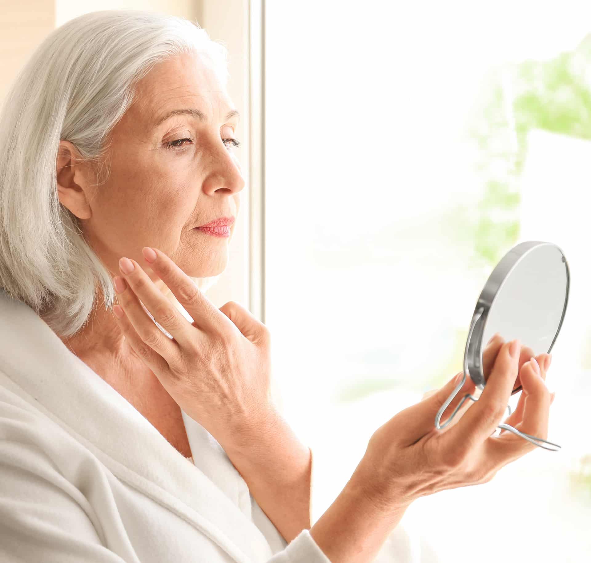 elder woman looking into a mirror after cosmetic skin treatment at halo skin institute