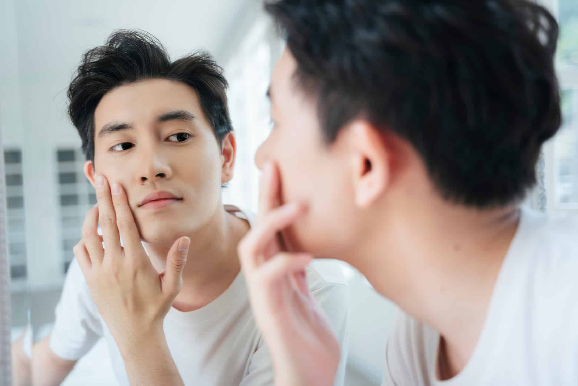 man looking in a mirror after medical dermatology treatment at halo skin institute